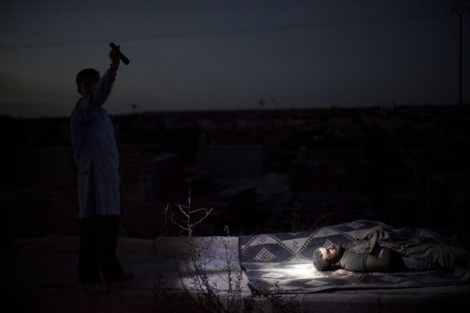 Egy férfi elemlámpával világít rá egy bombázás során elhunyt szíriai férfira.